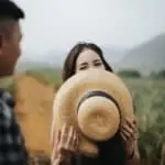 woman hides her smile with her hat